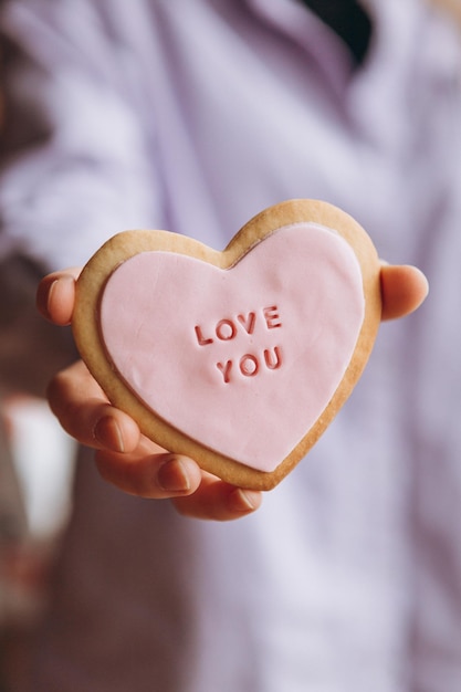 Ciasteczka w kształcie serca z różowym lukrem i napisem love you w rękach dziewczyny