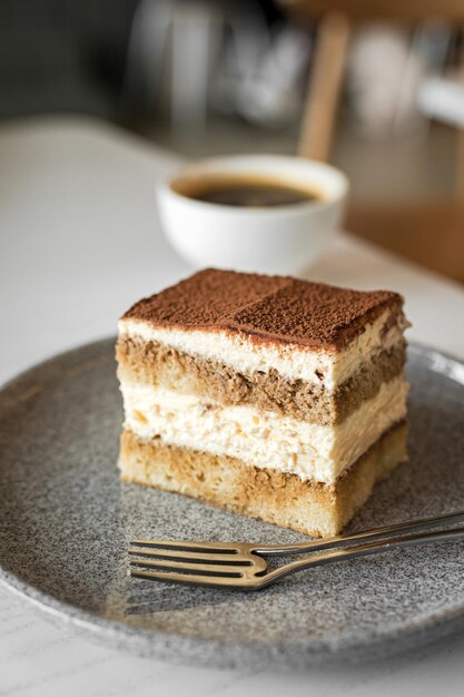 Ciasto deserowe Tiramisu na talerzu z widelcem i białą filiżanką czarnej kawy przy stole w kawiarni Styl życia obraz selektywna ostrość płytka głębia ostrości tło bokeh