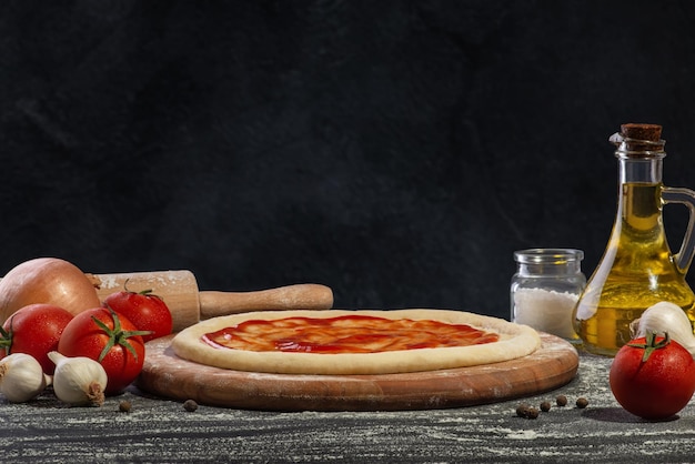 Ciasto do pizzy z sosem i innymi składnikami do robienia pizzy na czarnym tle