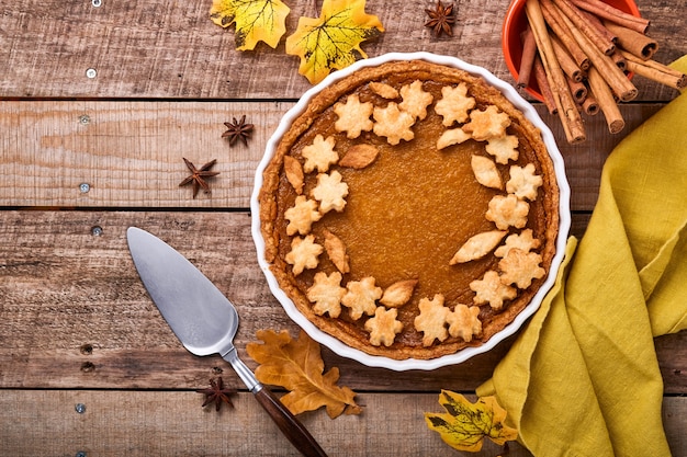 Ciasto dyniowe. Tarta z bitą śmietaną i cynamonem na rustykalnym tle. Tradycyjne amerykańskie domowe ciasto dyniowe na Święto Dziękczynienia lub Halloween Gotowe do spożycia. Makieta.