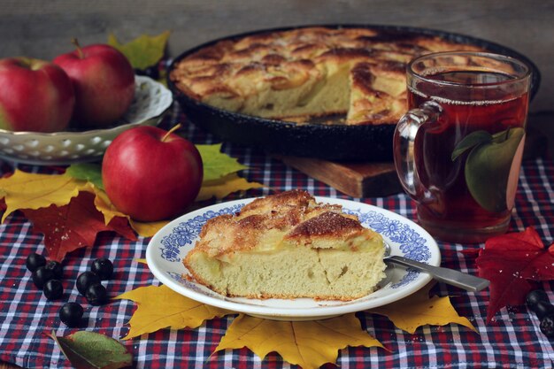 Ciasto jabłkowe. Charlotte. Kawałek ciasta na talerzu, filiżance herbaty i czerwonych jabłek