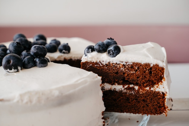 Zdjęcie ciasto jagodowe z kremem na biały drewniany stół kuchenny. ciasto z nadzieniem czekoladowym pokroić w plasterki.