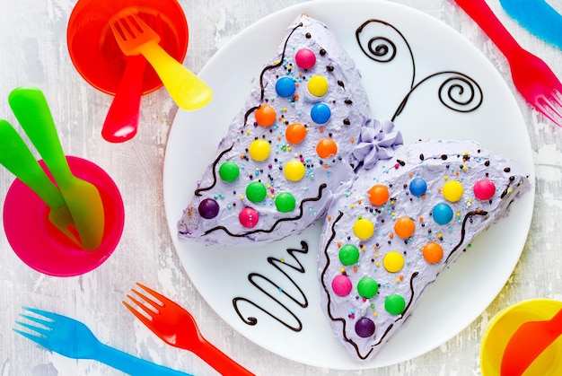 Ciasto motylkowe pyszne domowe ciasto w kształcie kolorowego motyla ozdobione kremową czekoladą i kolorowymi cukierkami