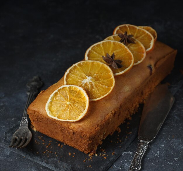 Ciasto pomarańczowe, ozdobione karmelizowanymi pomarańczami i kakao i cukrem pudrem na ciemnym kamiennym tle