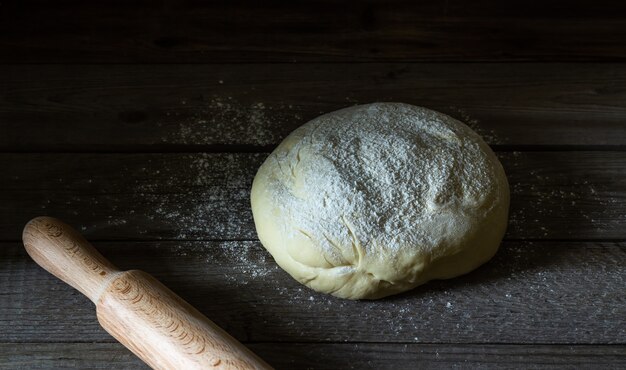 Ciasto posypuje się mąką na drewnianym.