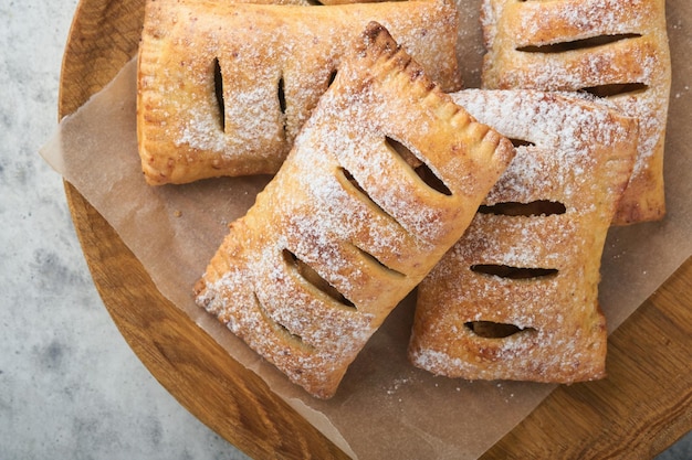 Ciasto ręczne Mini ciasto francuskie lub ciasta ręczne nadziewane jabłkiem i posypane cukrem pudrem w drewnianym talerzu Domowa przekąska z ciasta ze skórką na śniadanie rustykalne zdjęcie Kopiuj miejsce