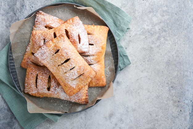 Ciasto ręczne Mini ciasto francuskie lub ciasta ręczne nadziewane jabłkiem i posypane cukrem pudrem w drewnianym talerzu Domowa przekąska z ciasta ze skórką na śniadanie rustykalne zdjęcie Kopiuj miejsce