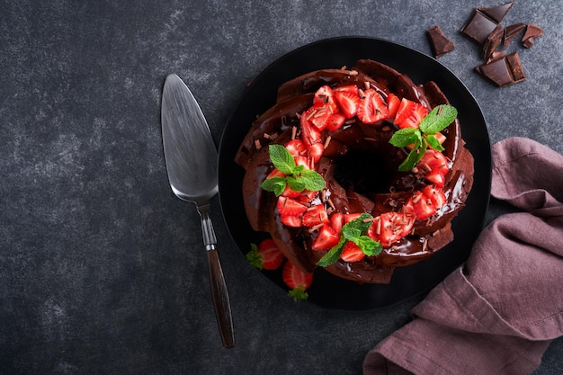 Ciasto z ciemnej czekolady Bundt z lukrem ganache i truskawkami na ciemnym tle kamiennego lub betonowego stołu Świąteczny tort Selektywna ostrość