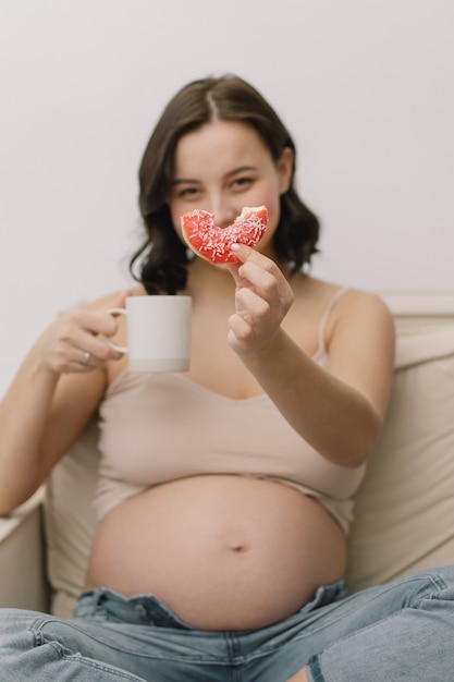 Ciąża i odżywianie. Kobieta w ciąży korzystających z pączków i herbaty. Pojęcie oczekiwań i zdrowia.