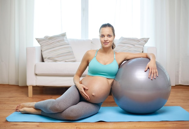 ciąża, sport, fitness, ludzie i koncepcja zdrowego stylu życia - szczęśliwa kobieta w ciąży ćwicząca z fitballem w domu