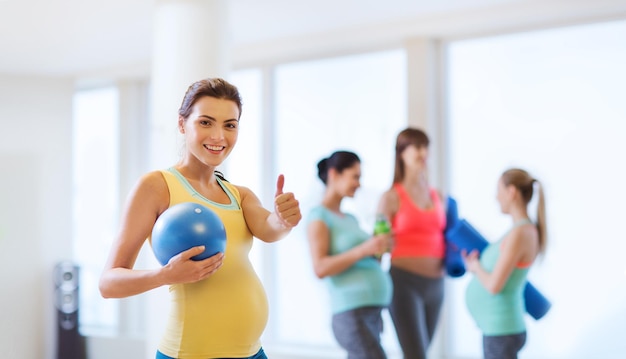ciąża, sport, fitness, ludzie i koncepcja zdrowego stylu życia - szczęśliwa kobieta w ciąży z piłką na siłowni pokazująca kciuki do góry