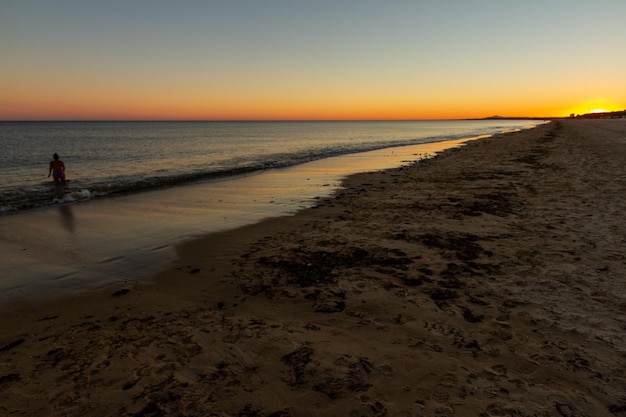 cicha hiszpańska plaża o zachodzie słońca, na której ludzie chodzą i biegają