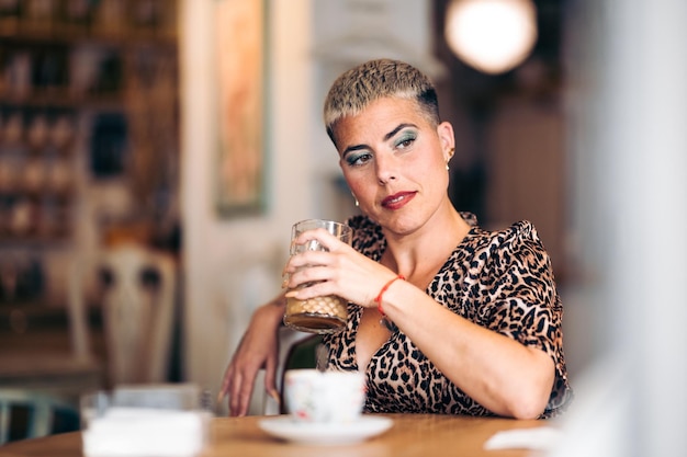 Zdjęcie ciekawa hipsterska kobieta patrzy z boku ze szklanką w barze