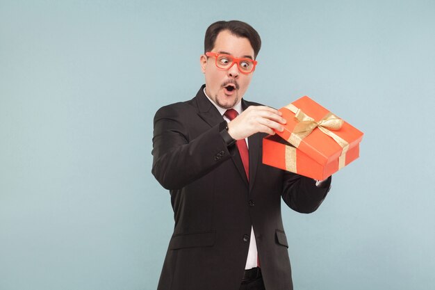 Ciekawy człowiek biznesu trzymający czerwone pudełko i zaglądający do środka