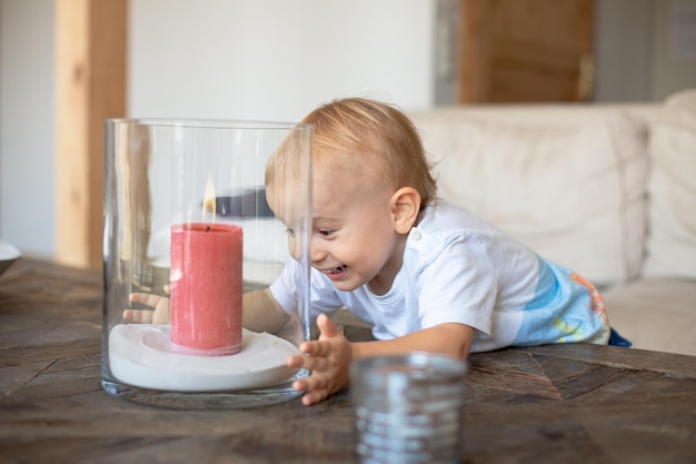 Ciekawy mały chłopiec bawi się kruchym szklanym wazonem z płonącą świeczką. Koncepcja bezpieczeństwa dziecka w domu.