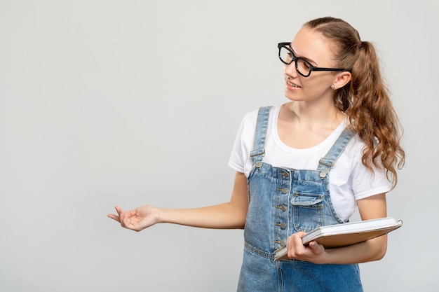 Ciekawy portret studenta Lekcja szkolna Wesoła inteligentna nastolatka w okularach z książkami uśmiecha się patrząc na miejsce na kopię na białym tle na jasnym tle Nowoczesna edukacja College seminarium