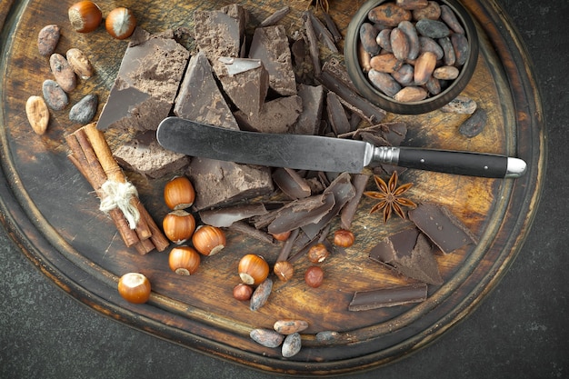 Ciemna czekolada w kompozycji z ziaren kakaowych i orzechów, na starym tle.