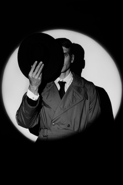 Ciemna sylwetka detektywa męskiego w płaszczu i kapeluszu w stylu noir Dramatyczny portret w stylu filmów detektywistycznych lat 50. Sylwetka szpiega w kręgu światła jak Agent 007