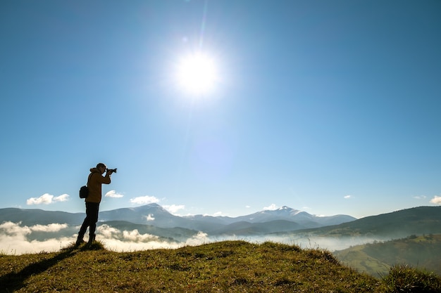Ciemna sylwetka fotografa turystycznego robiącego zdjęcie krajobrazu poranka w jesiennych górach.
