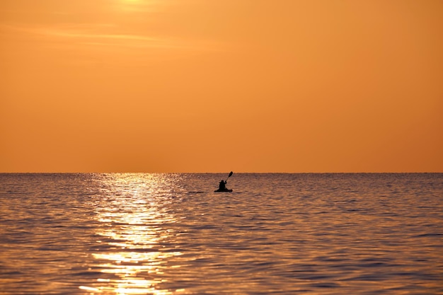 Ciemna sylwetka samotnego rybaka wiosłującego na swojej łodzi na wodzie morskiej o zachodzie słońca