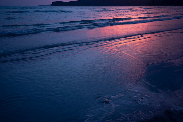 Ciemnego morza piaskowatej plaży i czerwonego światła słonecznego zmierzchu zmierzchu oceanu tło