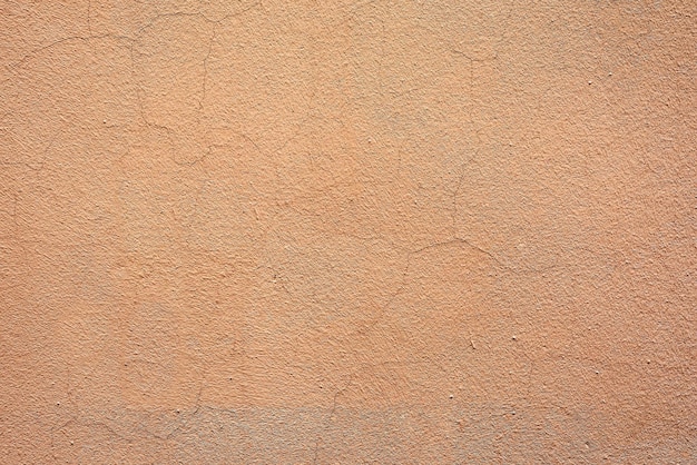 Ciemnobeżowy spękany tynk na ścianie budynku. Tekstura materiału wykończeniowego