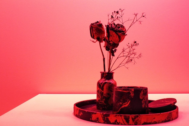 Ciemnoczerwone róże w wazonie i świeca na białym stole na różowej ścianie. Zen, relaks, koncepcja odnowy biologicznej.