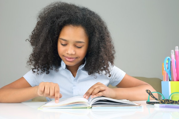 Ciemnoskóra uczennica czytająca książkę odrabiającą pracę domową. nauka w edukacji szkolnej