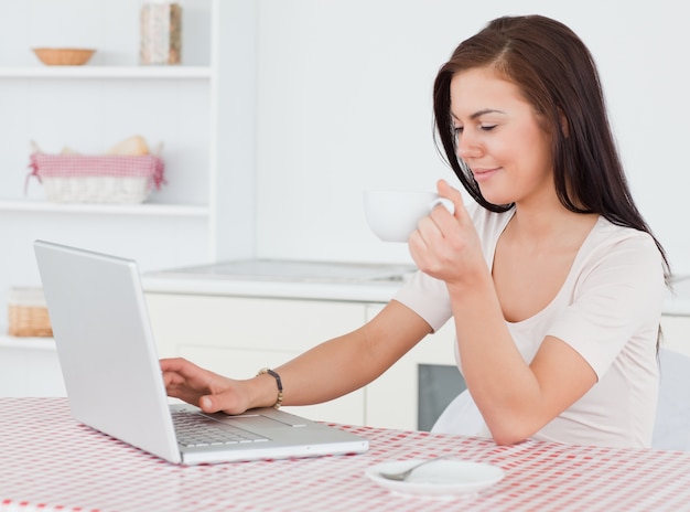 Ciemnowłosa kobieta używa jej laptop i mieć herbaty
