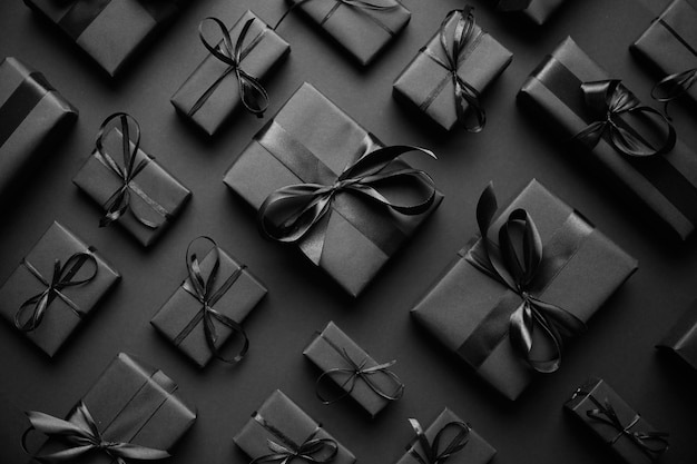 Zdjęcie ciemny temat świąteczny kwarteczne pudełko z prezentami zawinięte w czarny papier i wstążkę ułożone na czarnym tle płaski widok górny