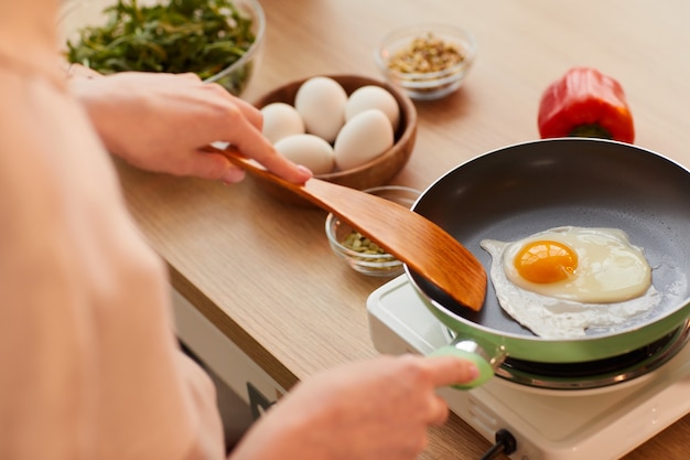 Ciepłe stonowanych bliska nie do poznania młoda kobieta gotowania jajek na patelni przygotowując zdrowe śniadanie rano