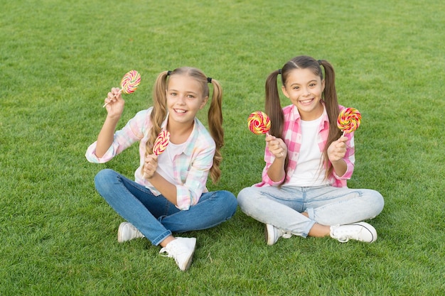 Ciesz się tymi lizakami z doznaniami smakowymi Szczęśliwe dzieci trzymają lizaki zielona trawa Jedzenie dużych lizaków wirujących na patykach Sklep ze słodyczami Ciesz się lizakami o owocowych smakach Smacznie i pysznie