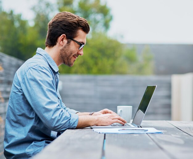 Cieszący się wolnością freelancera Ujęcie przystojnego młodego mężczyzny korzystającego z laptopa na zewnątrz