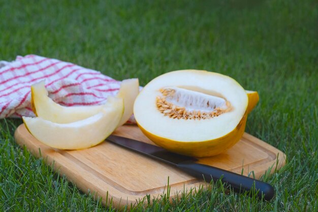 cięty melon leży na drewnianej desce obok niego leży czarny nóż i ręcznik w czerwonej klatce na grze