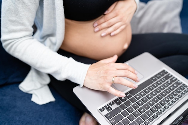 Ciężarna brunettre kobieta siedzi na kanapie w salonie dotykając swojego brzucha i rozmawiając z nią