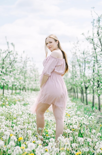 Ciężarna dziewczyna w różowej sukience w ogrodzie kwiatowym