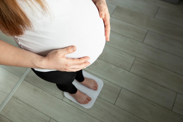 Ciężarną kobietę waży się na wadze łazienkowej