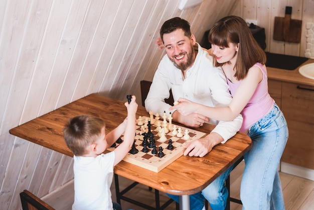 Ciężarna mama patrzy, jak tata i syn grają w szachy przy stole