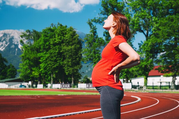 Ciężarna sportowa kobieta fitness cierpiąca na ból w dole pleców na stadionie sportowym