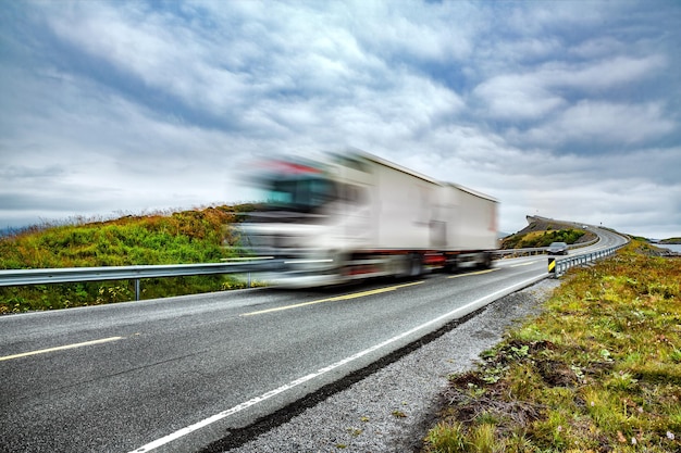 Zdjęcie ciężarówka i autostrada o zachodzie słońca. samochód ciężarowy w rozmycie ruchu. atlantic ocean road lub atlantic road (atlanterhavsveien) otrzymały tytuł „norweskiej budownictwa stulecia”.