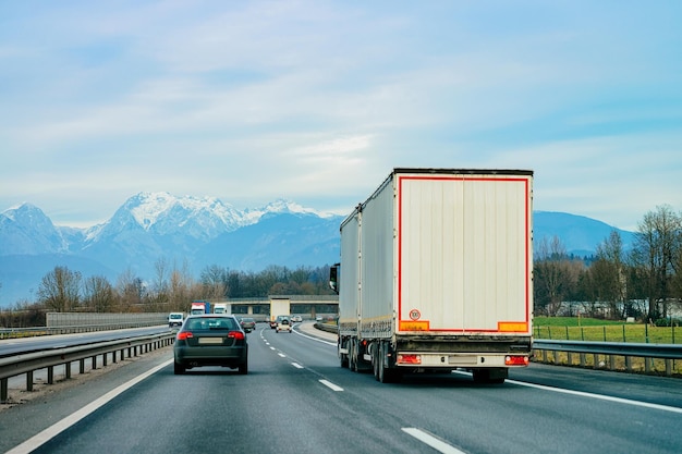 Ciężarówka na drodze. Kierowca ciężarówki na autostradzie. Ciężarówka wykonująca prace logistyczne. Naczepa z kierowcą. Duży samochód towarowy. Dostawa ładunku. Branża transportowa eksport. Kontener z załadowanym towarem na tle.