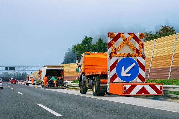 Ciężarówka przewożąca strzałkę w dół lewy kierunek odblaskowy znak drogowy na autostradzie w Polsce.