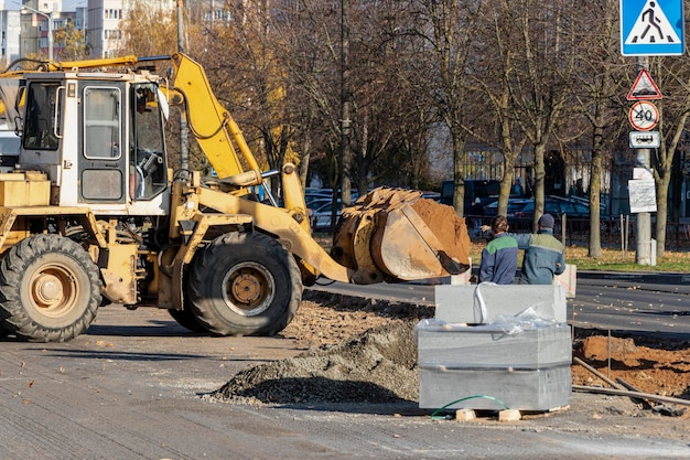 Ciężki ładowacz czołowy transportuje ziemię w łyżce i wyrównuje drogę. Jesienią remont drogi w centrum nowoczesnego miasta. Ciężkie maszyny budowlane do przenoszenia gleby.