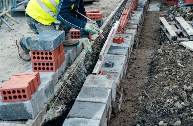 Ciężko pracujący murarz układający betonowe bloki na betonowym fundamencie na domu mieszkalnym