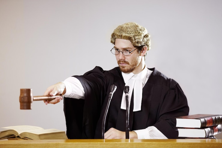 Zdjęcie cisza poważny młody sędzia siedzący na sali sądowej z surowym wyrazem twarzy, trzymającym młotek