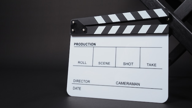 Zdjęcie clapperboard lub clap board lub tabliczka filmowa z krzesłem reżyserskim w produkcji wideo, filmie, przemyśle kinowym na czarnym tle.