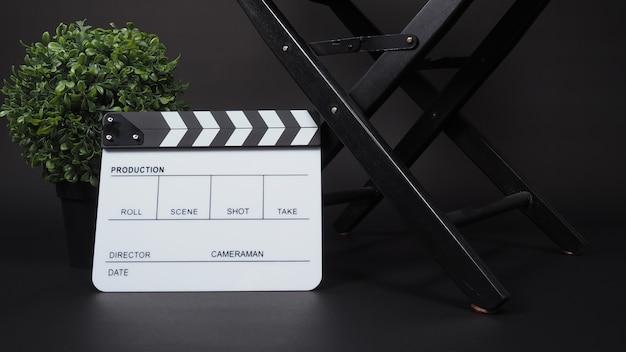 Clapperboard lub clap board lub tabliczka filmowa z krzesłem reżyserskim w produkcji wideo, filmie, przemyśle kinowym na czarnym tle.