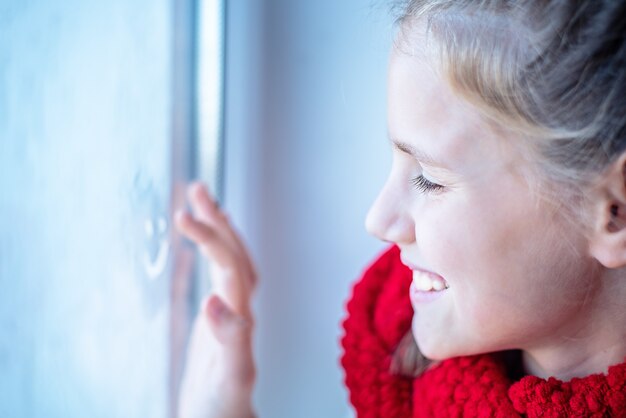 Zdjęcie close-up portret dziewczynki rysującej wesoły emoji na szybie okna. selektywna ostrość obrazu.