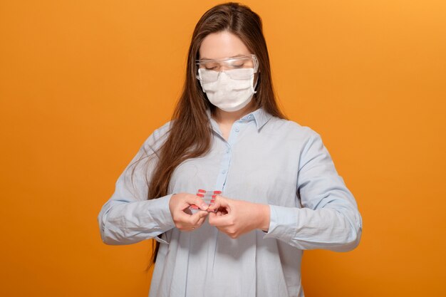 Close-up portret młodej kobiety w ochronnej masce medycznej z objawem koronawirusa, pigułki w dłoniach, kaszel i gorączka, pandemia wirusa koronawirusa