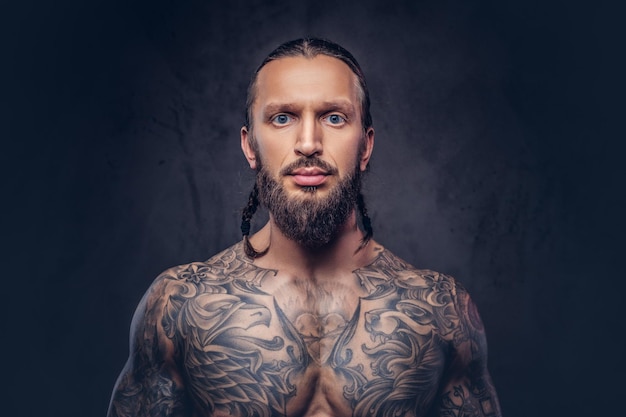 Close-up portret muskularnego brodatego mężczyzny tattoed ze stylową fryzurą. Na białym tle na ciemnym tle.